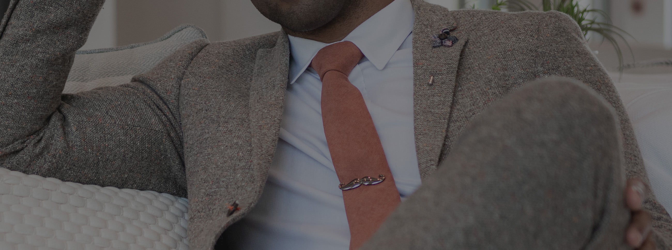 Man wearing a tan suit and burnt orange tie sitting down