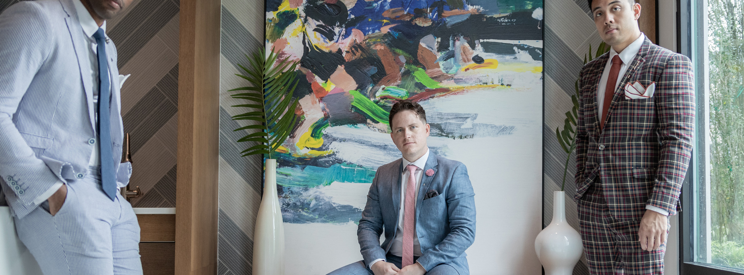 3 men wearing suits and ties standing in front of a large piece of artwork