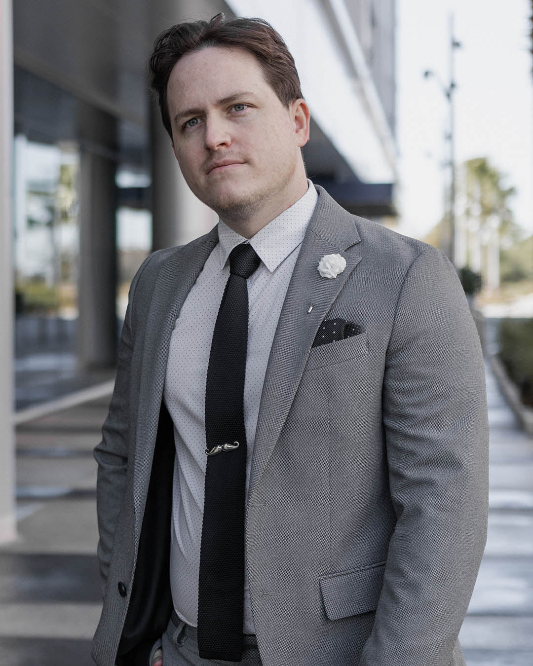 Man wearing a gray suit and black knitted tie in an urban setting. 