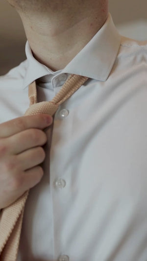 Man putting on the knitted sand tie set with a tan suit and white shirt